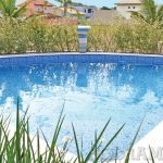 Uma piscina azul cintilante cercada por uma vegetação exuberante com edifícios residenciais ao fundo sob um céu claro.