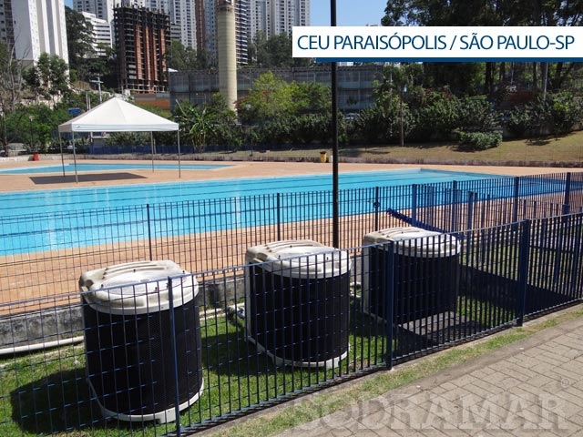Uma piscina externa cercada por uma cerca preta da Sodramar no ceu paraisópolis em São Paulo, Brasil, com grandes edifícios residenciais visíveis ao fundo.