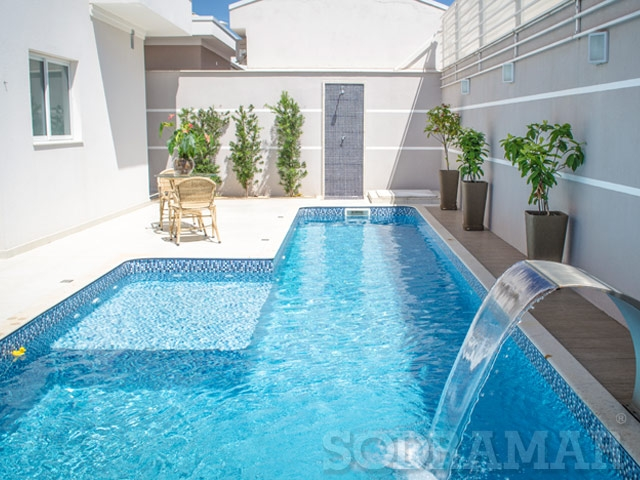 Piscina azul em forma retangular com uma castata em uma casa